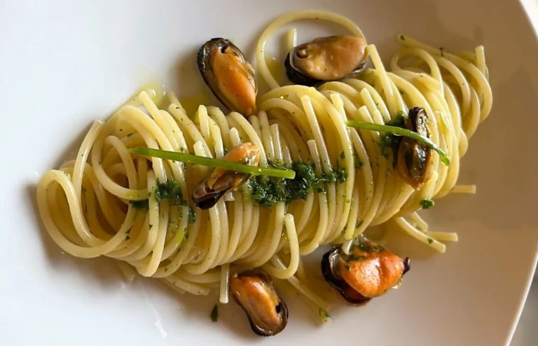 Spaghetti con cozze e prezzemolo su piatto bianco.